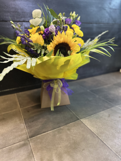 Golden Glow - Brighten someone's day with the `Golden Glow` arrangement, featuring a stunning sunflower mix with seasonal blooms. Complemented by lush green foliage, this arrangement brings a touch of nature's radiant beauty into any space.